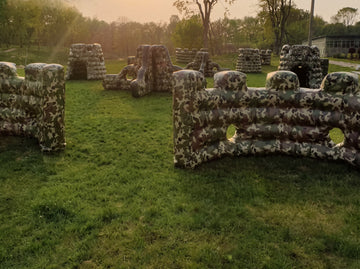 Inflatable airsoft bunker field with multiple camo bunkers set up on grass